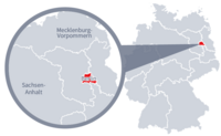 Diese Grafik zeigt eine Karte von Deutschland mit einer detaillierten Ansicht der Region Berlin. Berlin ist in Rot hervorgehoben und liegt im östlichen Teil Deutschlands. Ein Lupensymbol vergrößert diesen Bereich, um die Lage genauer darzustellen. 
